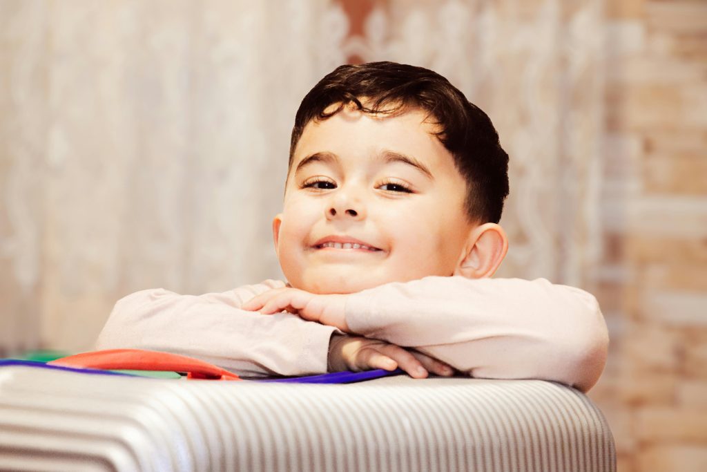 Cheerful Child Resting on a Suitcase Indoors